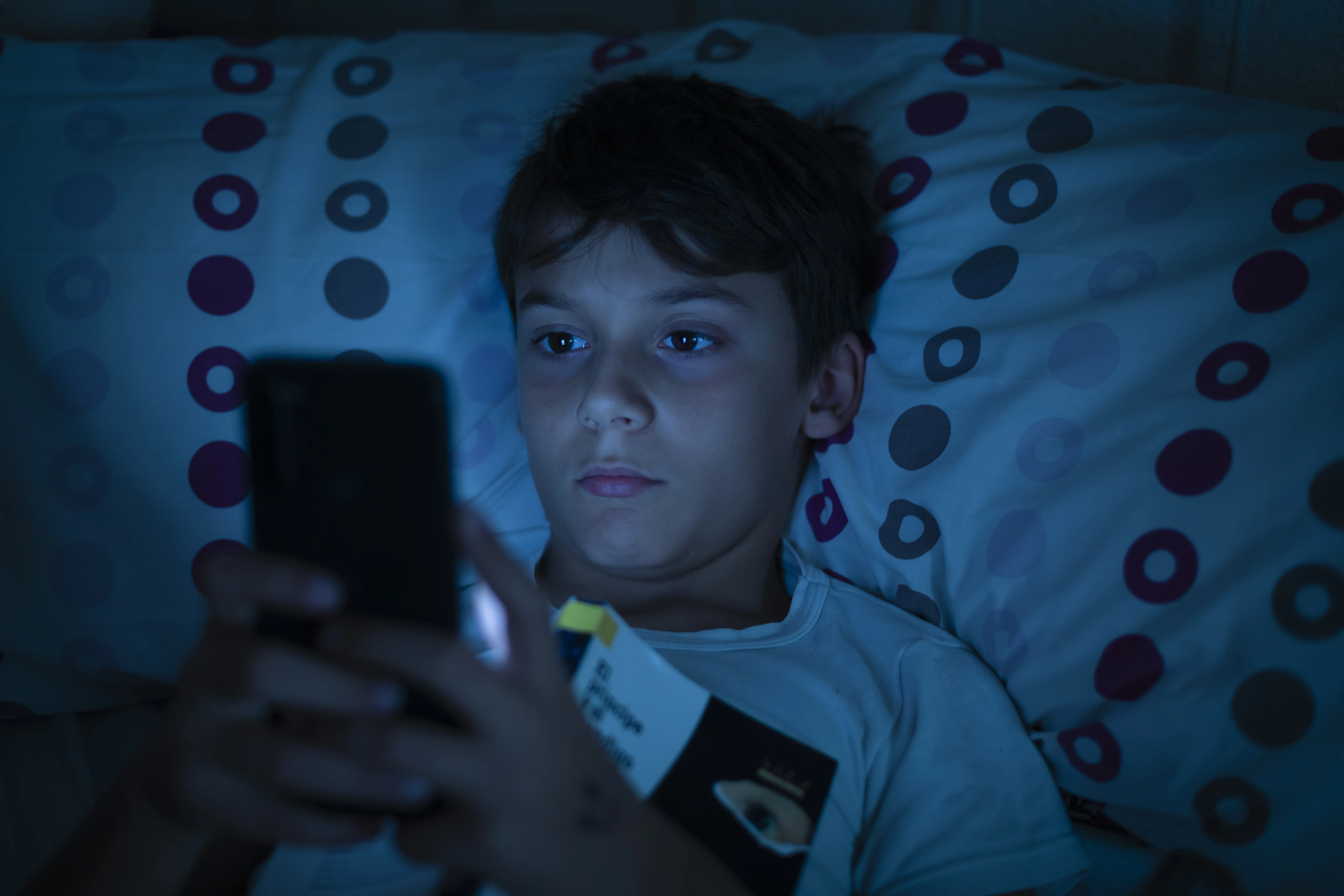 Dreng ligger i mørket i seng og kigger på mobiltelefon