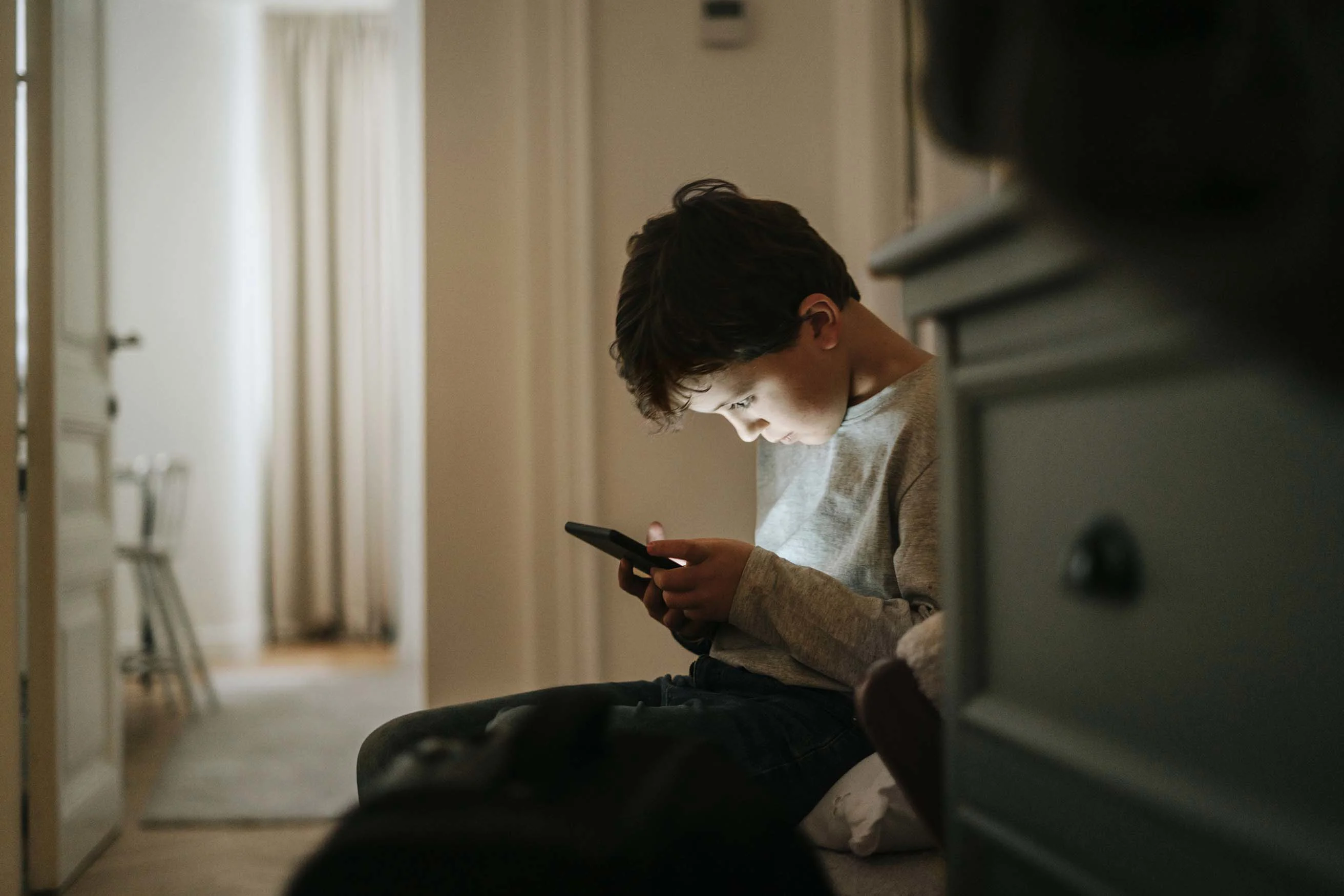 Dreng sidder med bøjet hoved og kigger på mobil