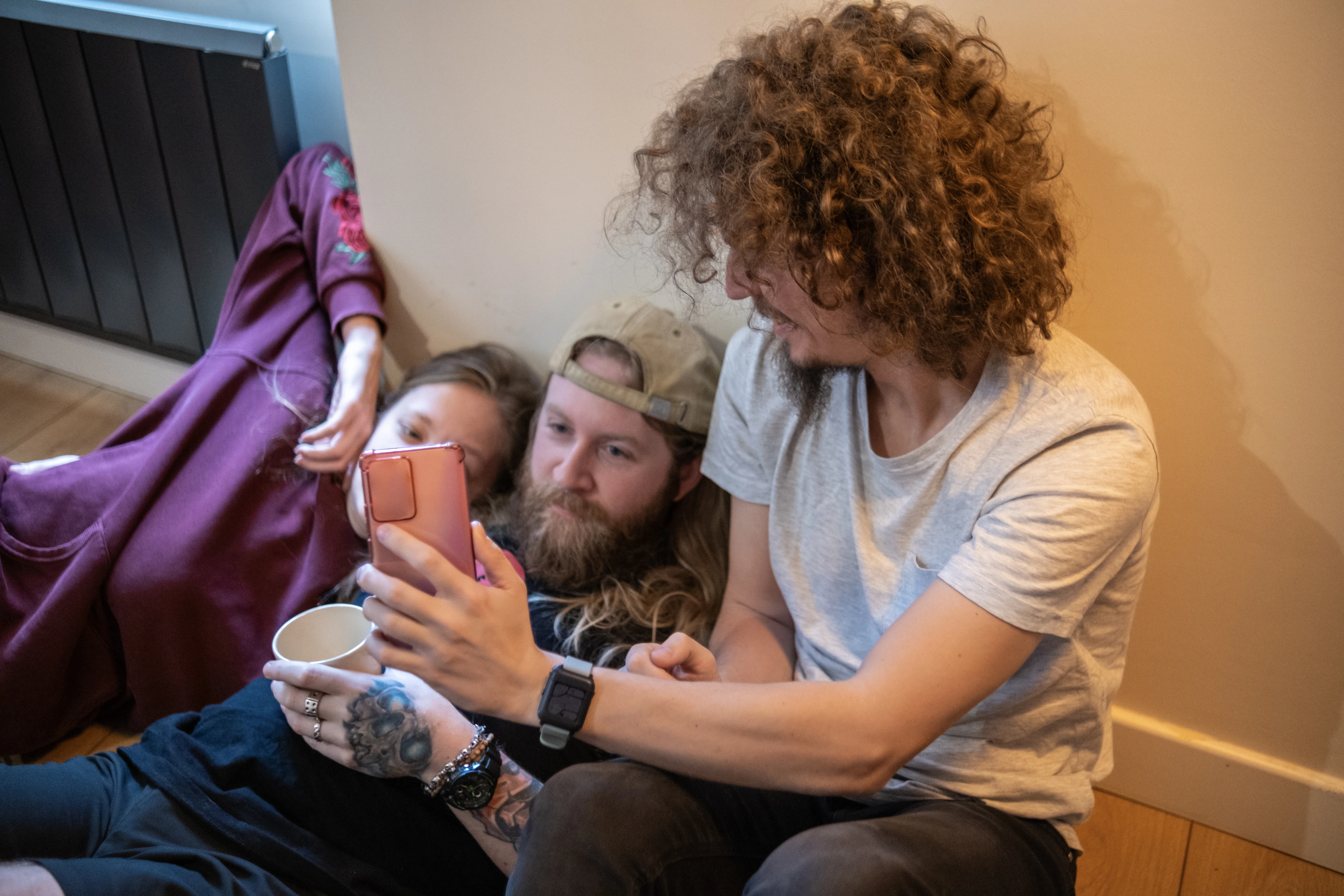 Far og datter ligger og slapper af på gulvet, mens en mand viser dem noget på sin smartphone