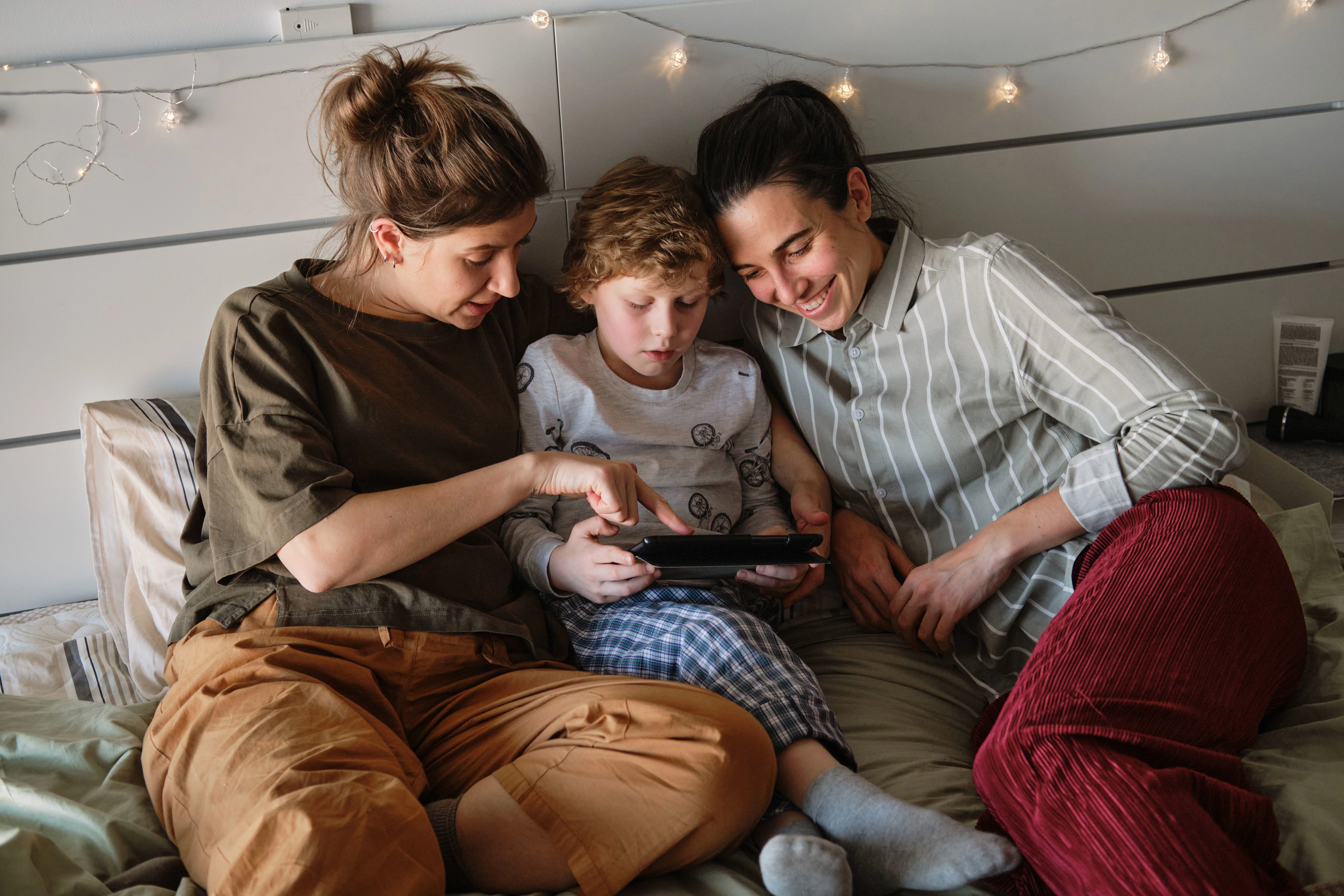 To mødre taler med deres søn om noget på en smartphone, som han holder.