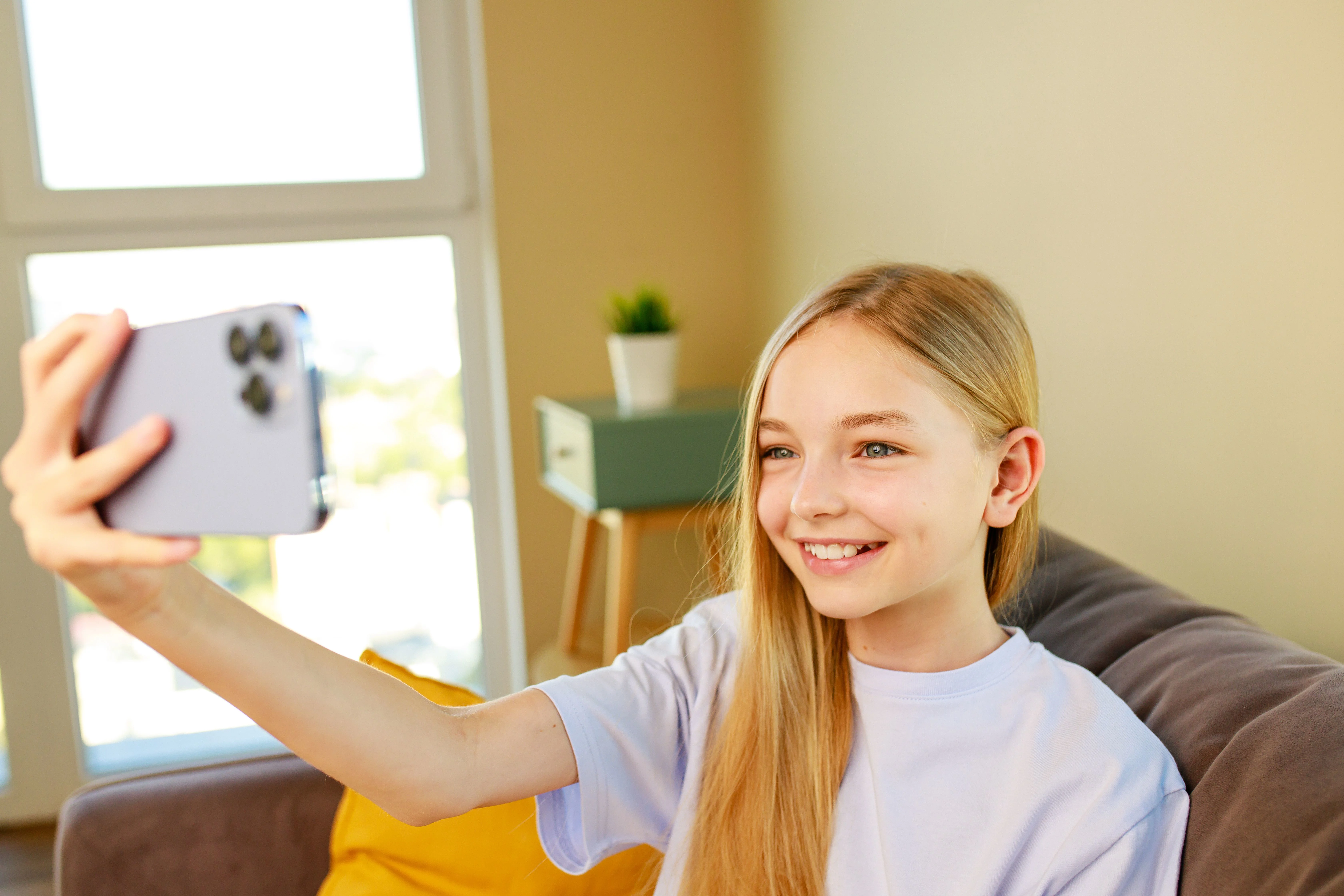 Ung pige smiler og tager selfie i sofa.