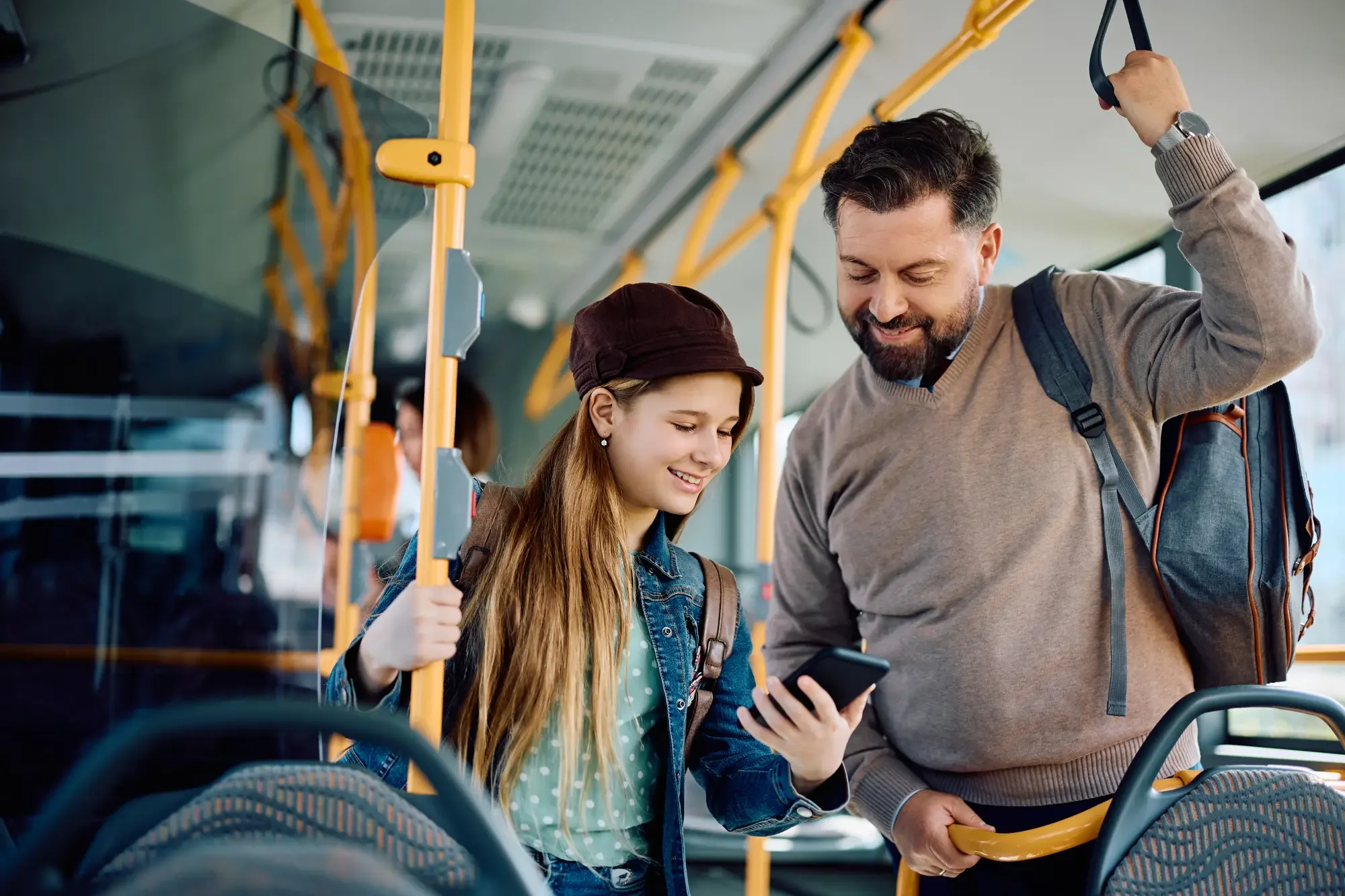 Datter og far står i bussen og kigger på datterens smartphone sammen, mens de smiler.
